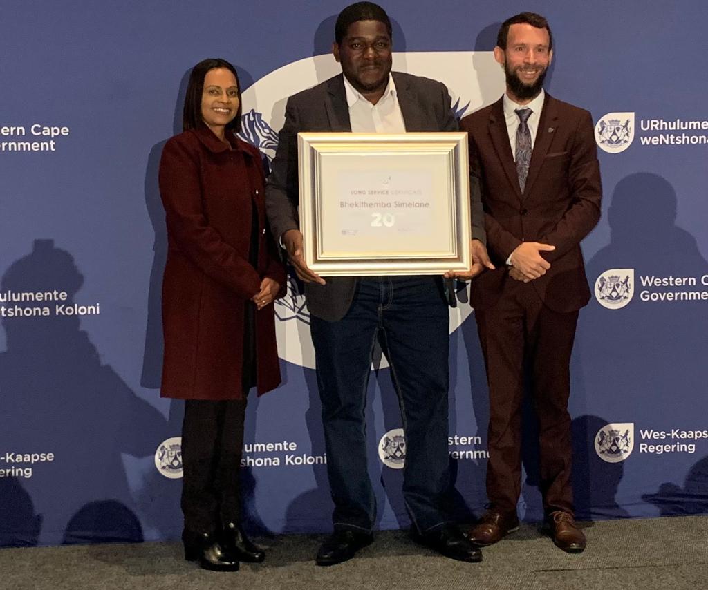 Head of Department (HOD), Adv Yashina Pillay; Centre: Director: Monitoring and Evaluation, Mr Bhekithemba Simelane receiving his 20-year service award, Right: Minister Reagen Allen