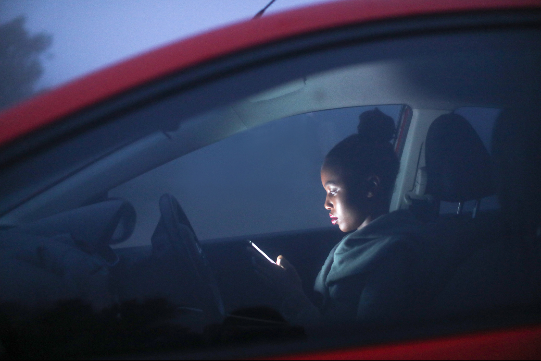 A young woman sitting in her car in the dark with her phone on 