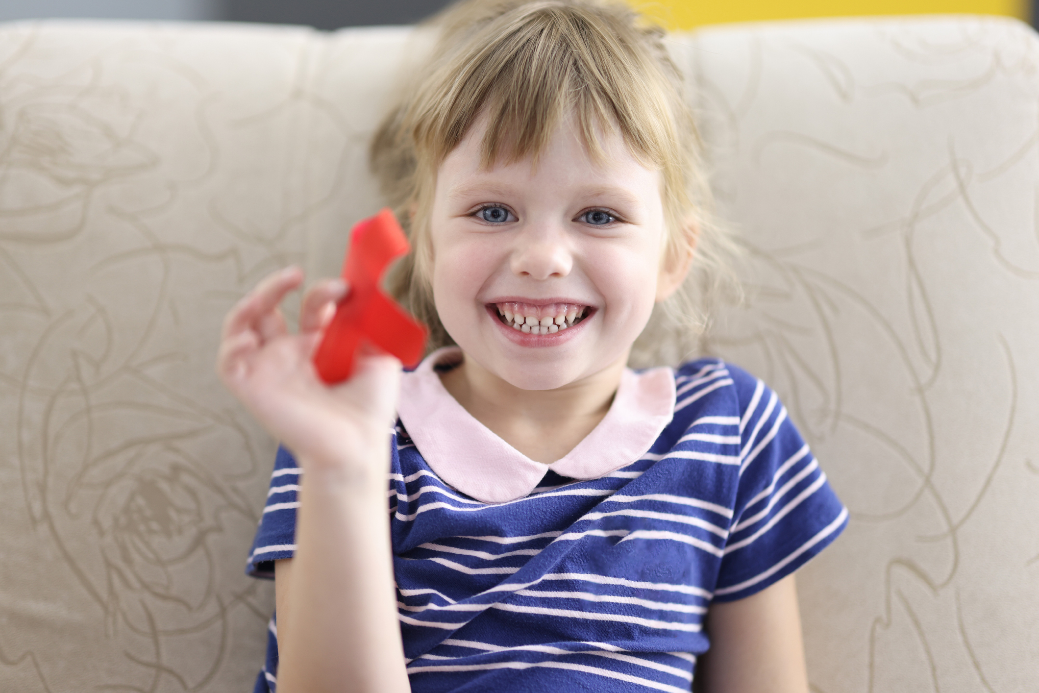 Little girl smiles and holds in her hand a red ribbon