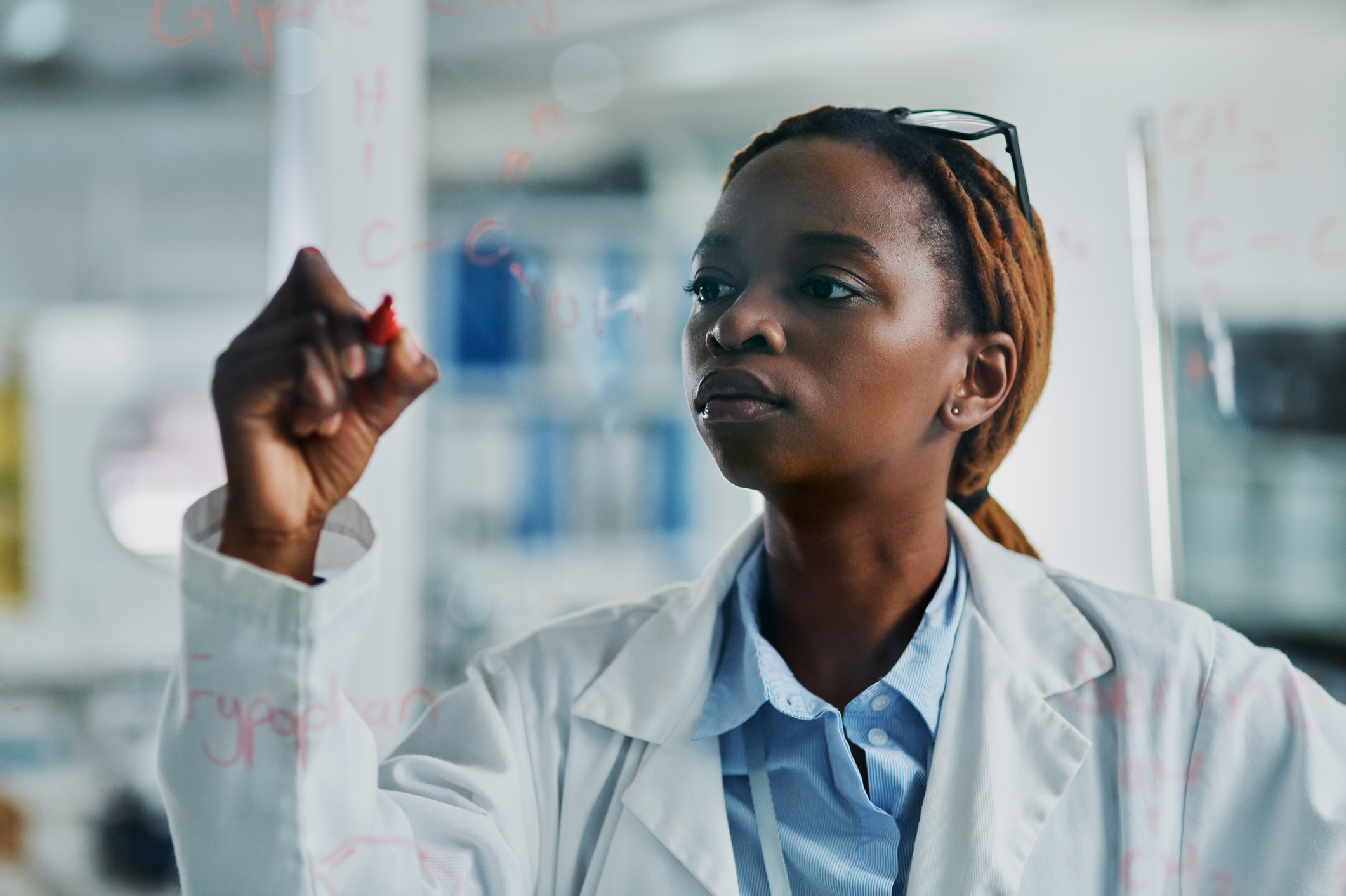A young female scientist writing on a glass wall while working in a laboratory