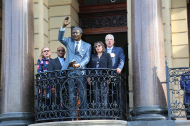 Dignitaries singing the national anthem on the City Hall balcony