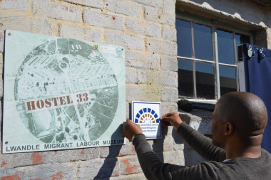Johathan Windvogel from Heritage Western Cape places the tile on the wall of the Hostel 33