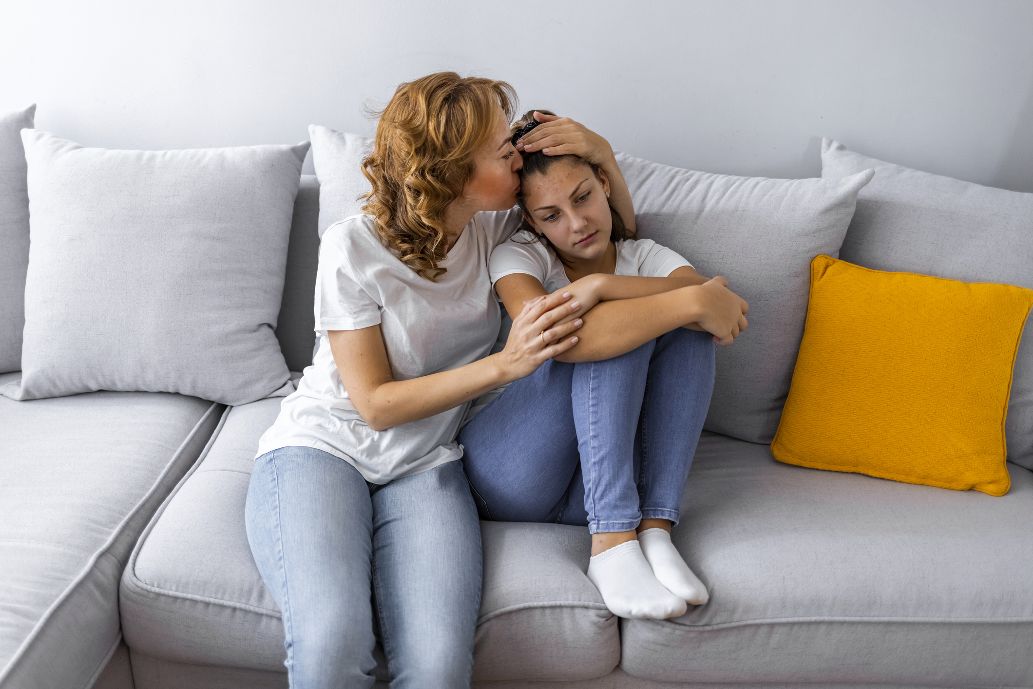 A caring mother hugs and comforts her teenage daughter on the couch